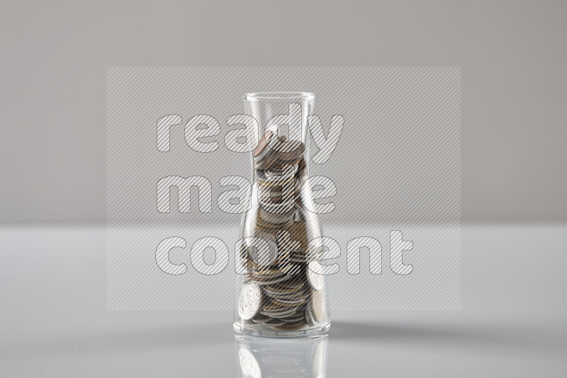 Random old coins in a glass jar on grey background