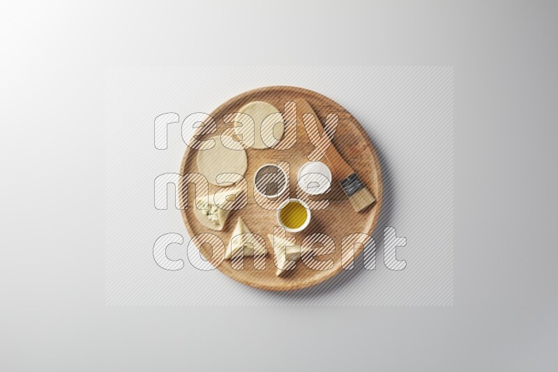 two closed sambosas and one open sambosa filled with cheese while salt, black pepper and oil with oil brush aside in a wooden dish on a white background