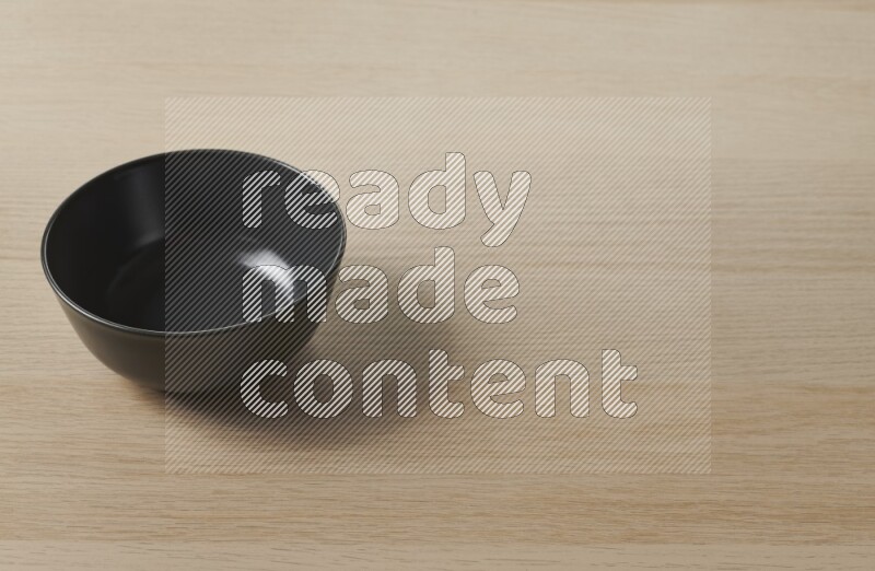 A black ceramic bowl on light wooden background
