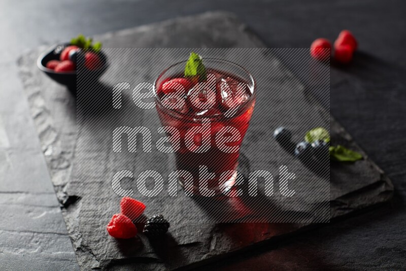 A glass of mixed berries juice with mint leaves on black background