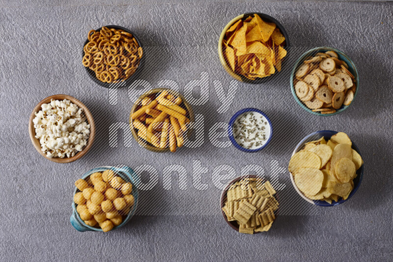Assorted snacks in pottery bowls on grey background