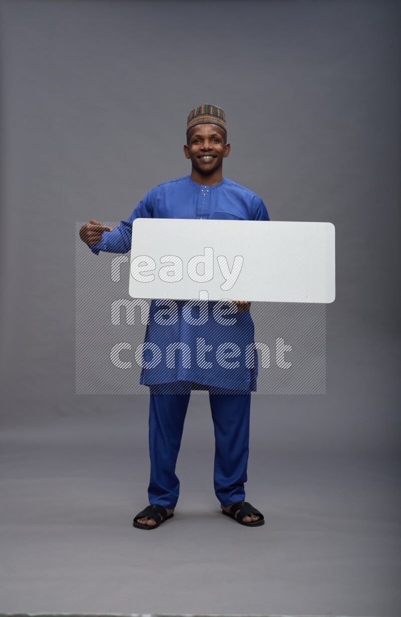 Man wearing Nigerian outfit standing holding board on gray background