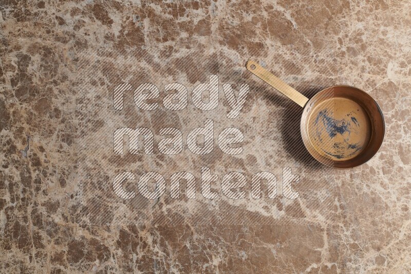 A small copper pan on beige marble background