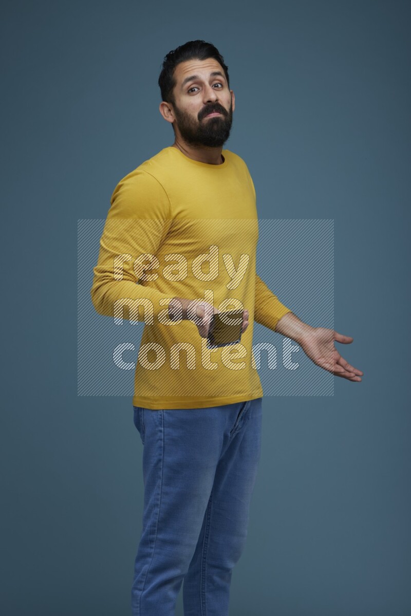 Man posing with a phone in a blue background wearing a yellow shirt