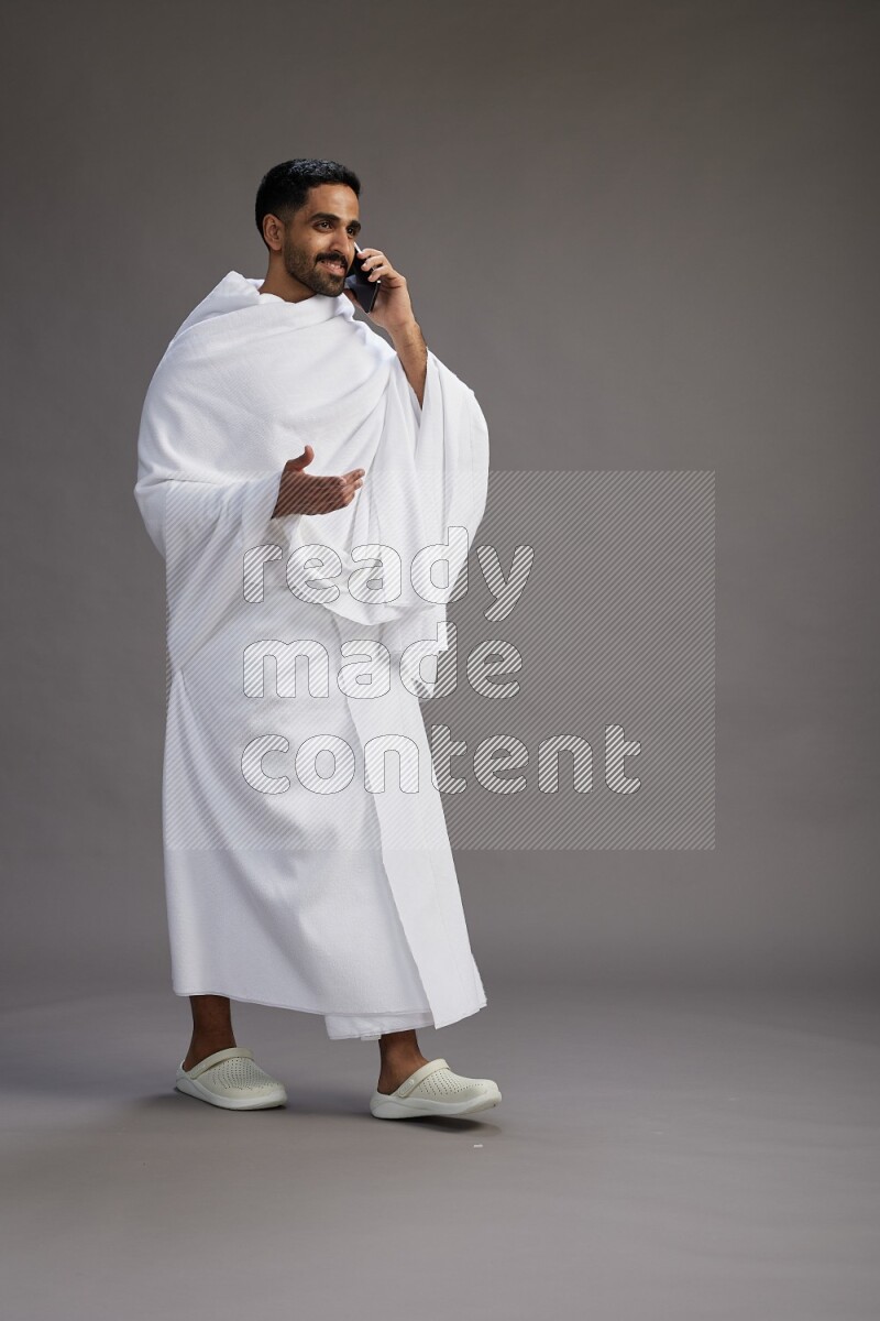 A man wearing Ehram Standing talking on phone on gray background