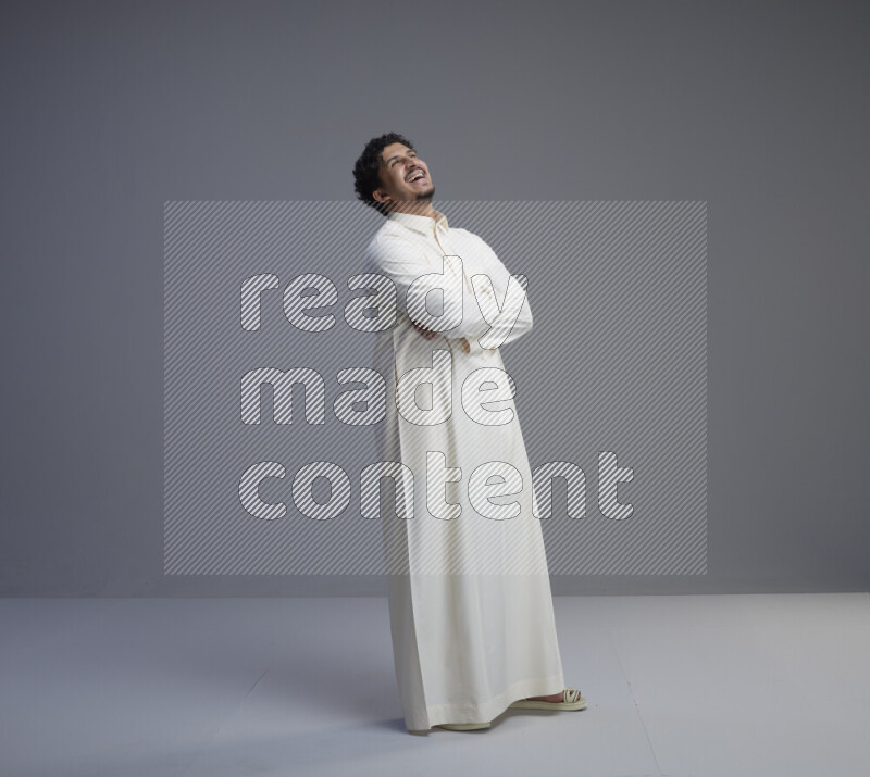 A Saudi man standing wearing thob interacting with the camera on gray background