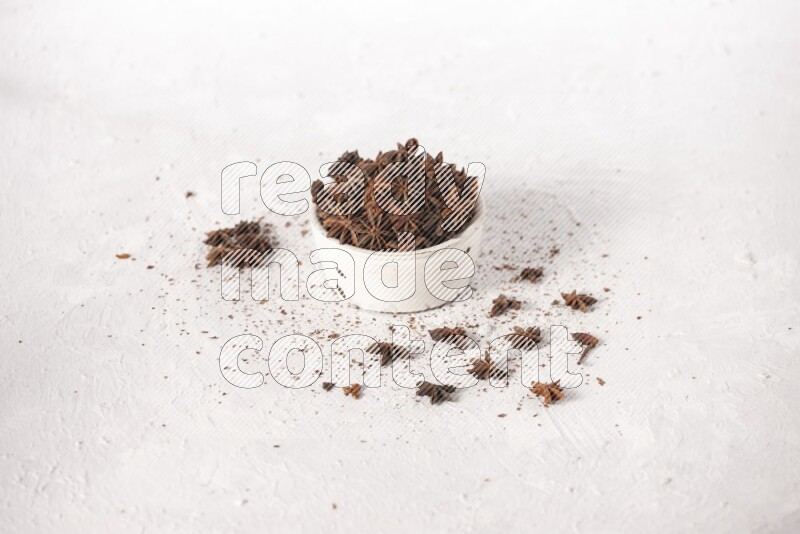 Star Anise in a white bowl and more of it sprinkled on white background
