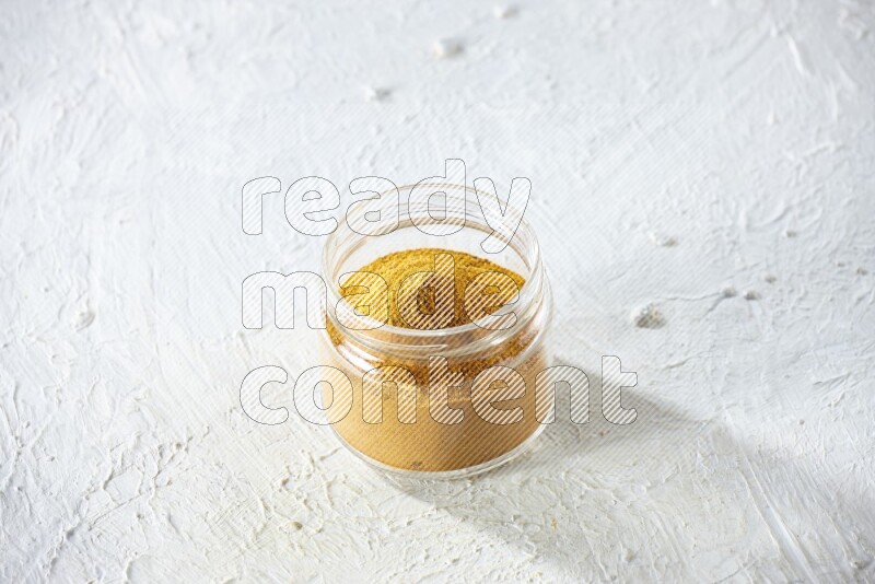 A glass jar full of turmeric powder on a textured white flooring