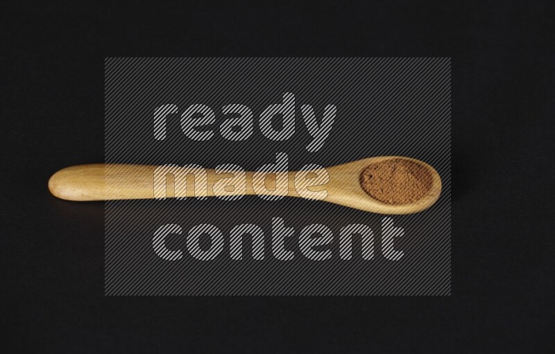 Cinnamon powder in a wooden spoon on a black background