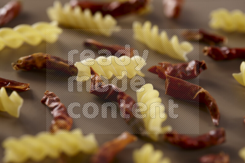 Raw pasta with different ingredients such as cherry tomatoes, garlic, onions, red chilis, black pepper, white pepper, bay laurel leaves, rosemary and cardamom on beige background