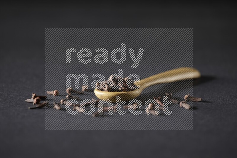 حبوب القرنفل في ملعقة خشبية وبعض من الحبوب تناثرت بخارجها علي خلفية سوداء