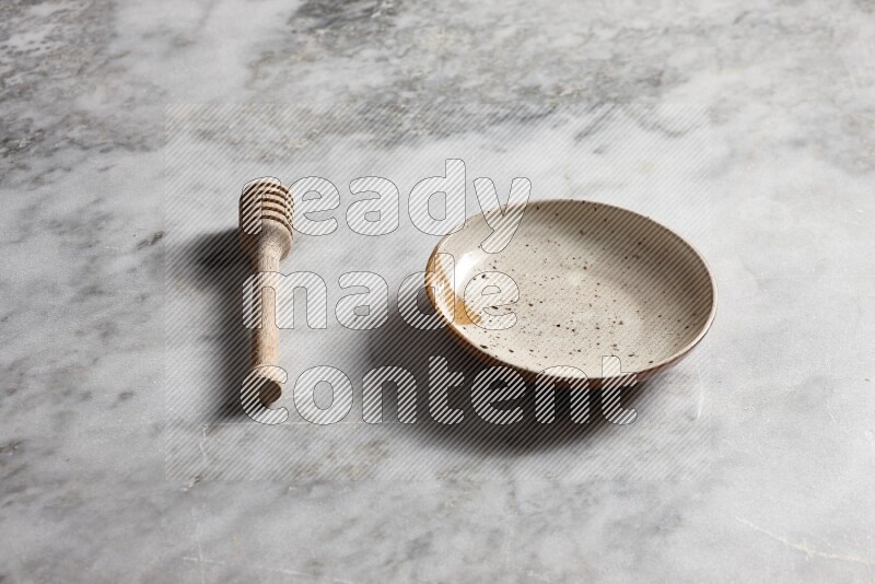 Multicolored pottery plate with wooden honey dipper on the side on grey marble background