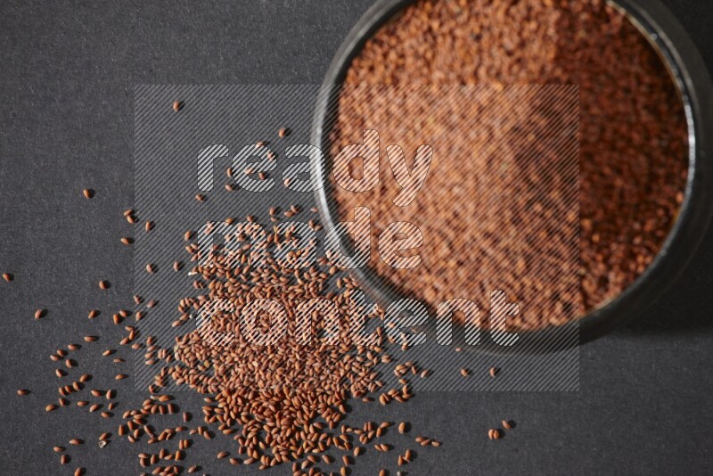 A black pottery bowl full of garden cress seeds on a black flooring