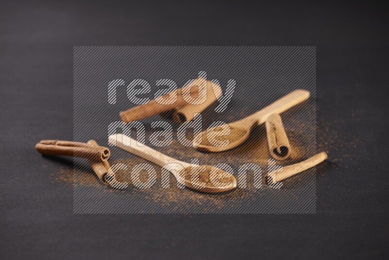 Cinnamon powder in two wooden spoons with cinnamon sticks on black background