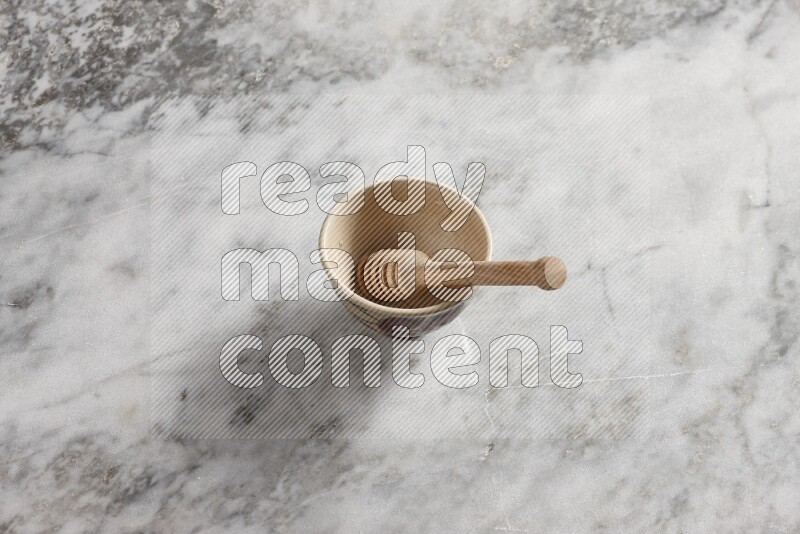 Decorative pottery bowl with wooden honey dipper in it on grey marble background