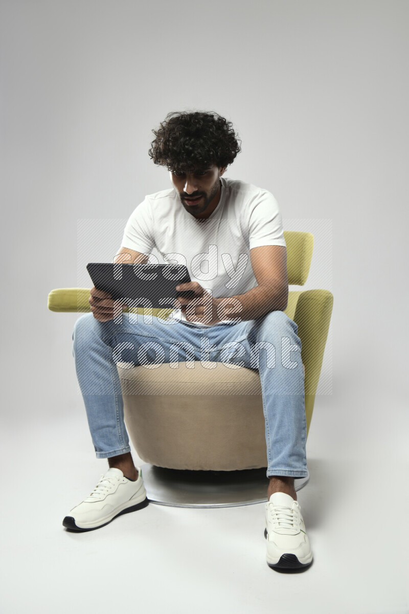 A man wearing casual sitting on a chair gaming on a tablet on white background