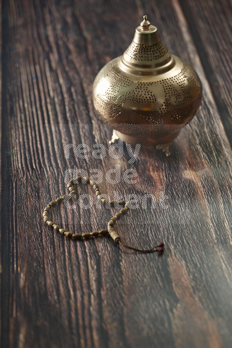 A golden lantern with different drinks, dates, nuts, prayer beads and quran on brown wooden background