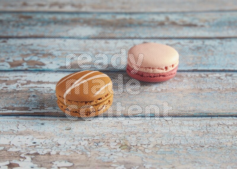 45º Shot of of two assorted Brown Irish Cream, and Pink Litchi Raspberry macarons on light blue background