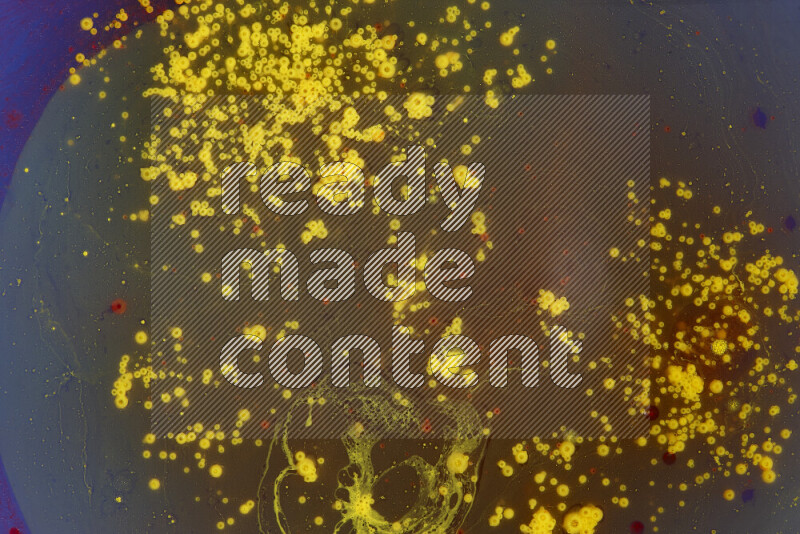 The image captures a dramatic splatter of yellow and red paints over an blue backdrop