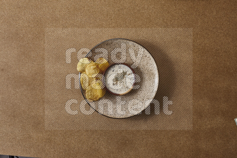 Assorted snacks on a pottery plate with a dipping on brown background