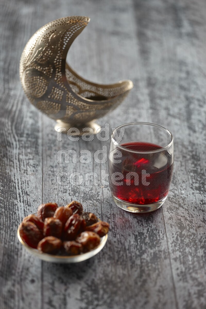 A silver lantern with different drinks, dates, nuts, prayer beads and quran on grey wooden background