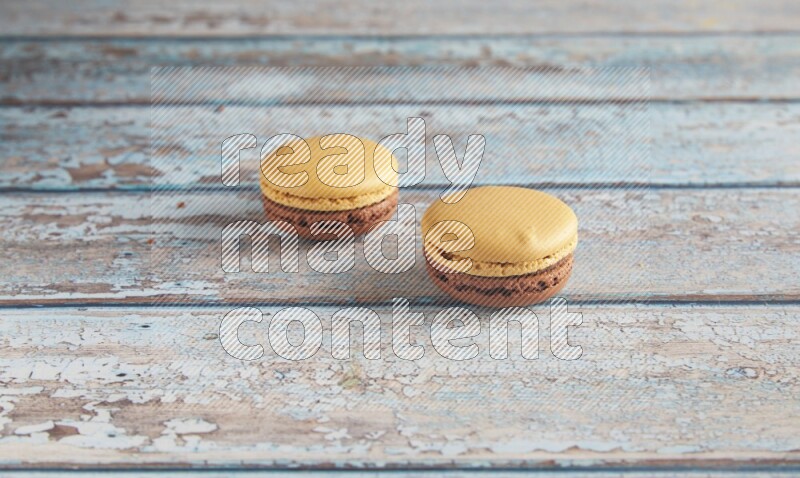 45º Shot of two Yellow and Brown Chai Latte macarons on light blue wooden background