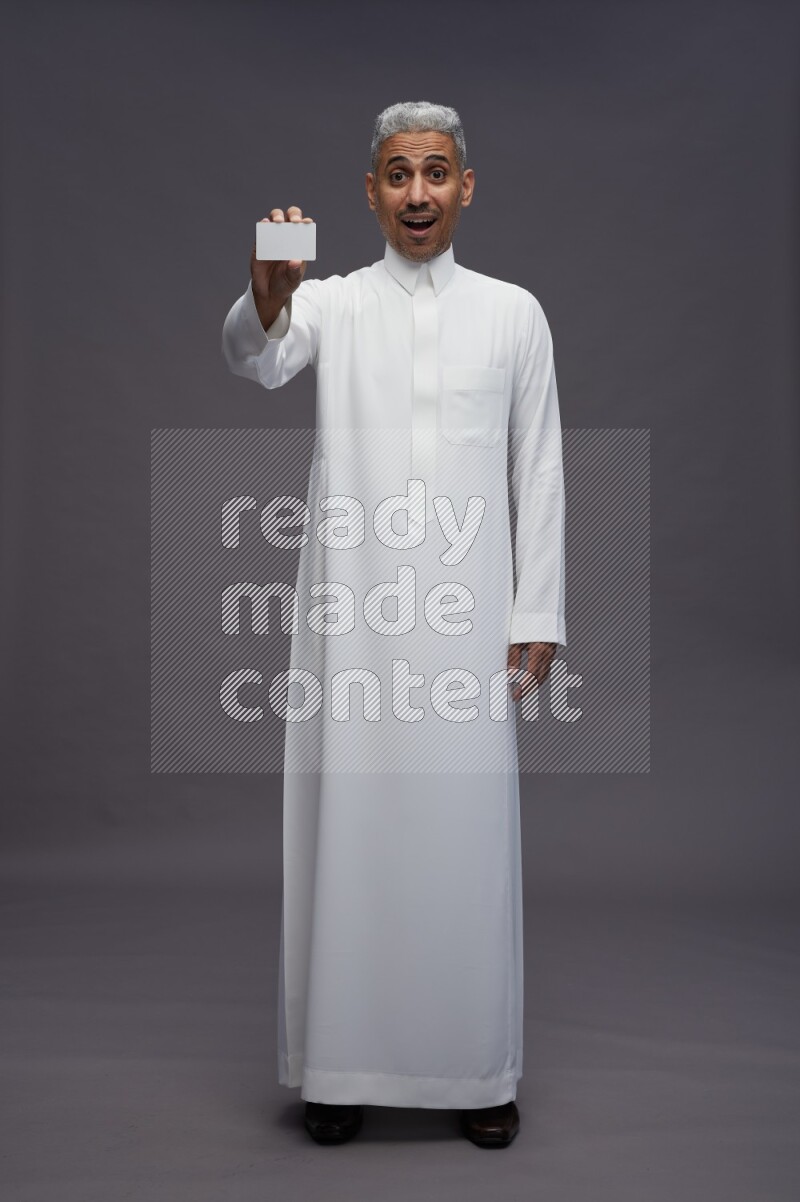 Saudi man wearing thob standing holding ATM card on gray background