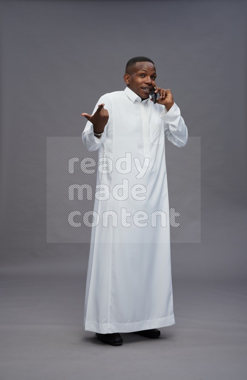Saudi man wearing thob standing talking on phone on gray background