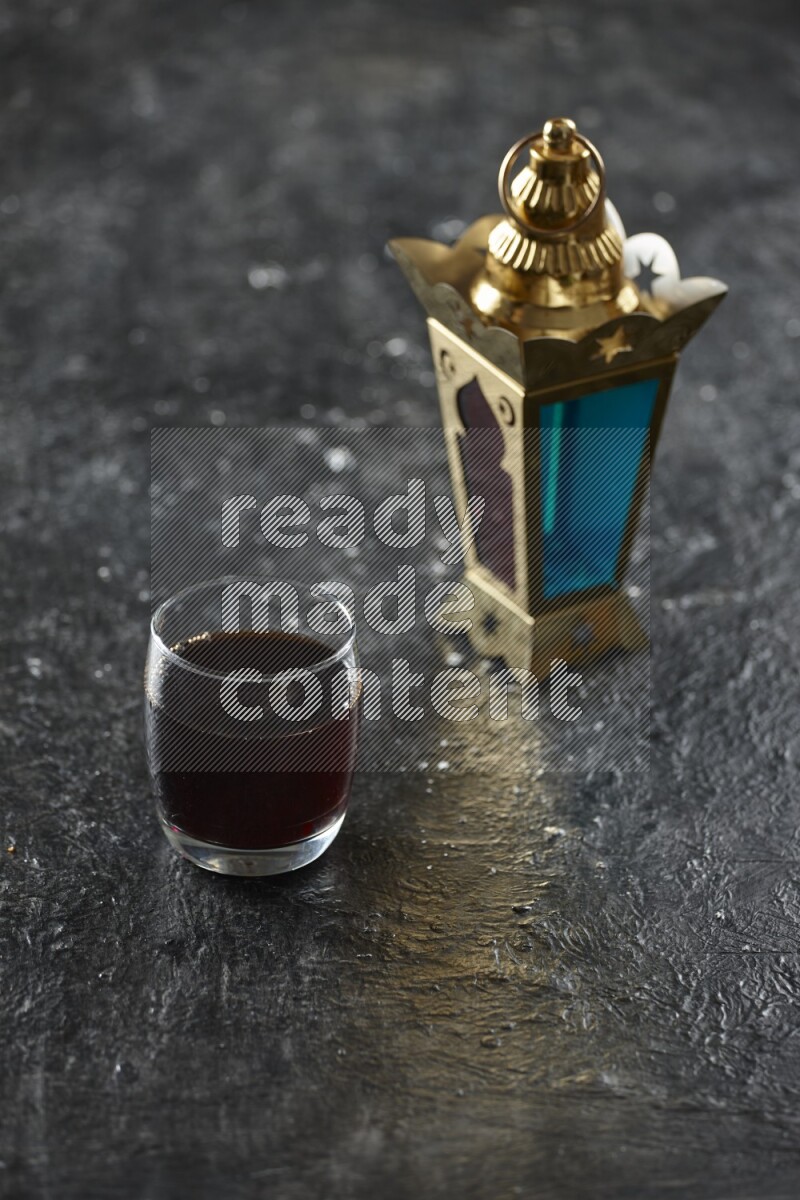 A golden lantern with different drinks, dates, nuts, prayer beads and quran on textured black background