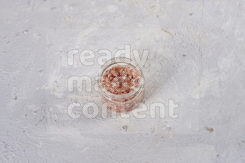 A glass jar full of coarse himalayan salt crystals on white background
