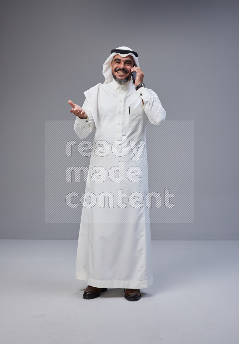 Saudi man Wearing Thob and white Shomag standing talking on phone on Gray background