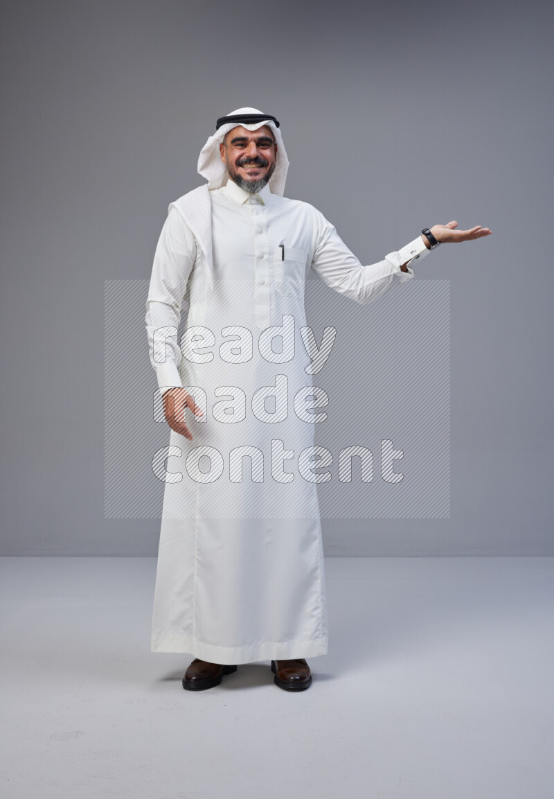Saudi man Wearing Thob and white Shomag standing interacting with the camera on Gray background