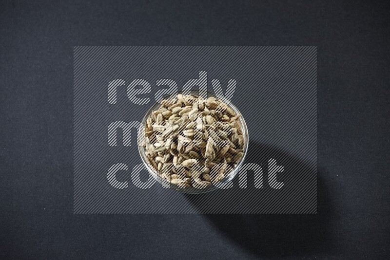 A glass bowl full of cardamom on black flooring