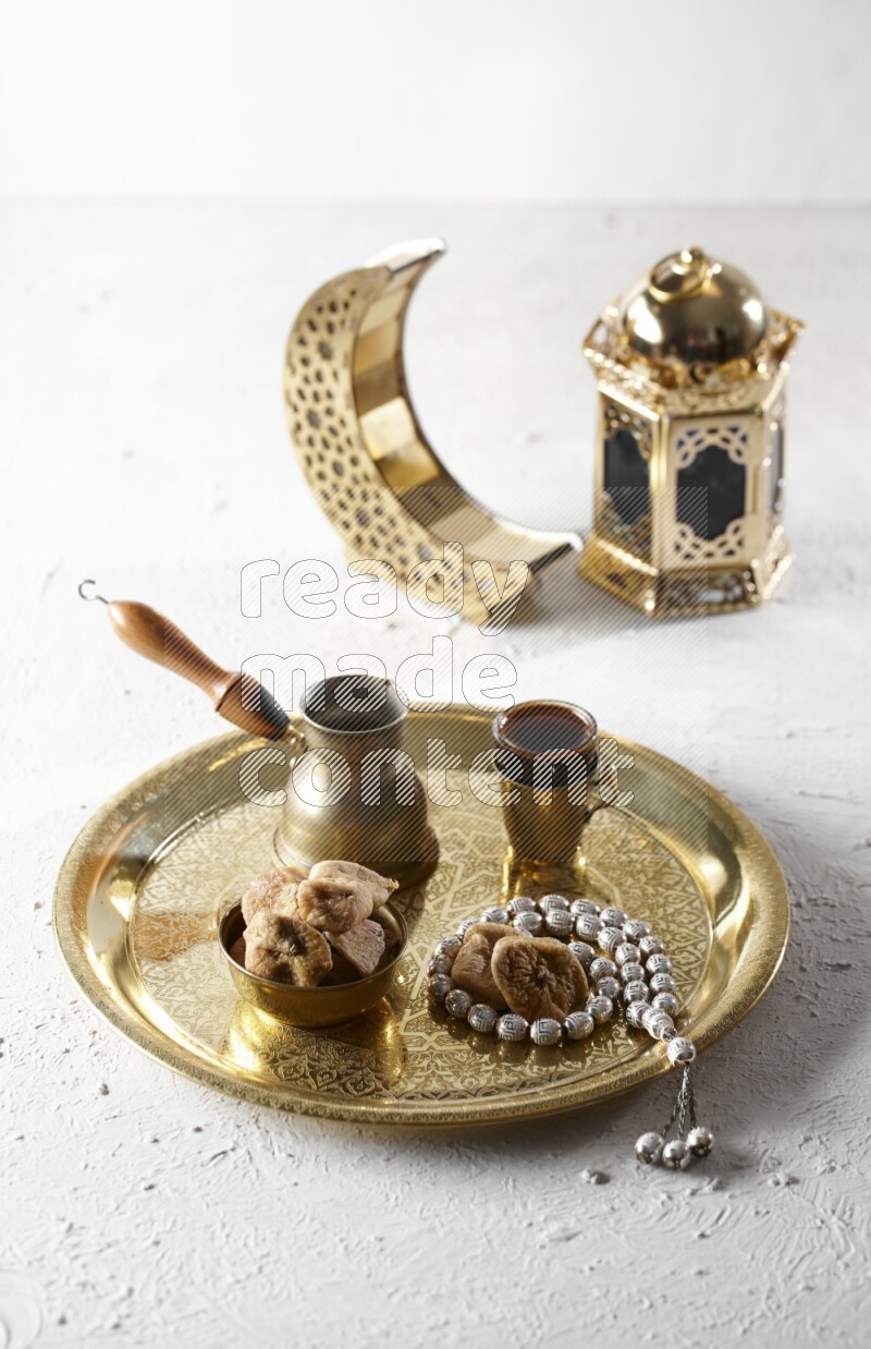 Dried figs in a metal bowl with coffee and prayer beads on a tray beside lanterns in a light setup