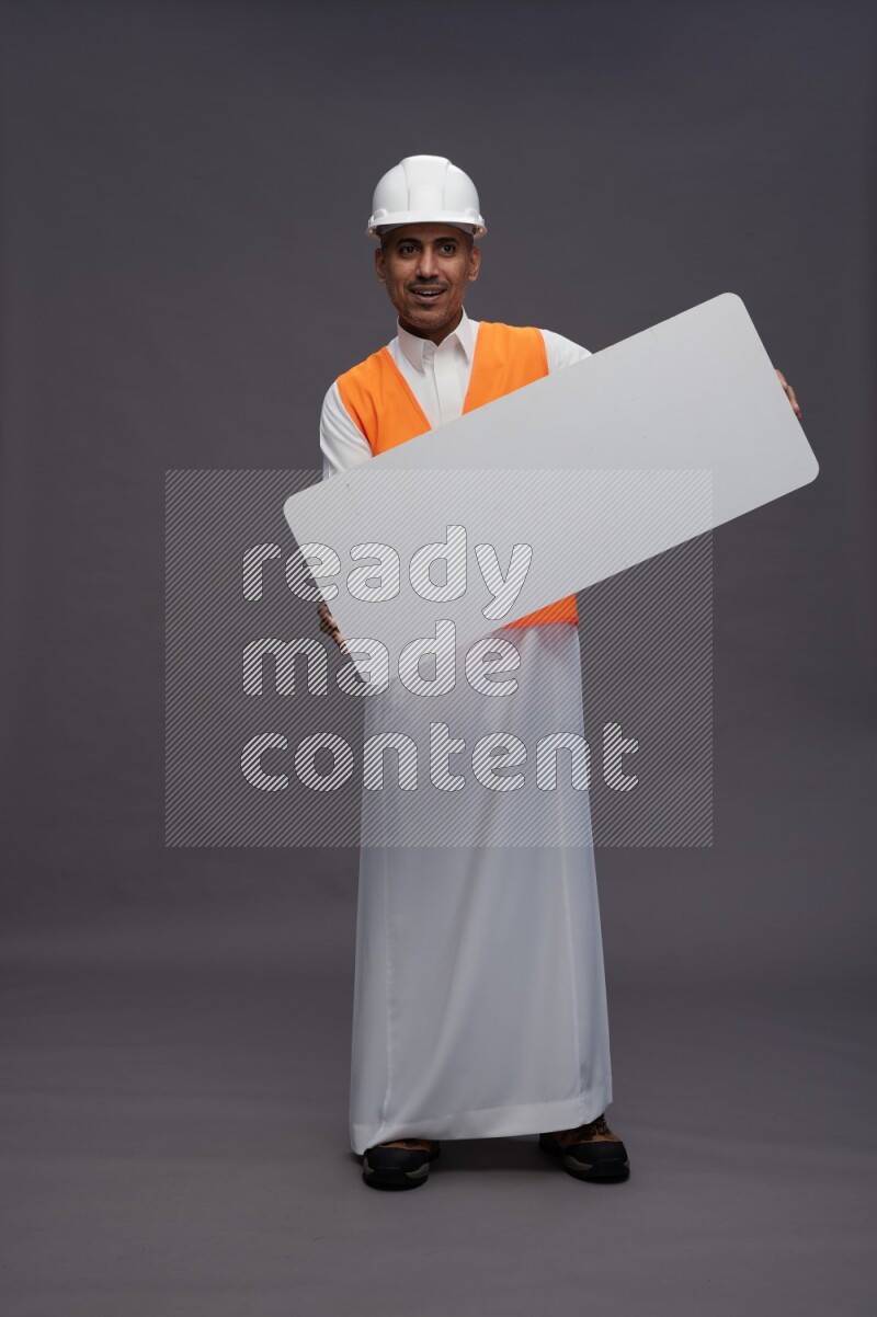 Saudi man wearing thob with engineer vest standing holding board on gray background