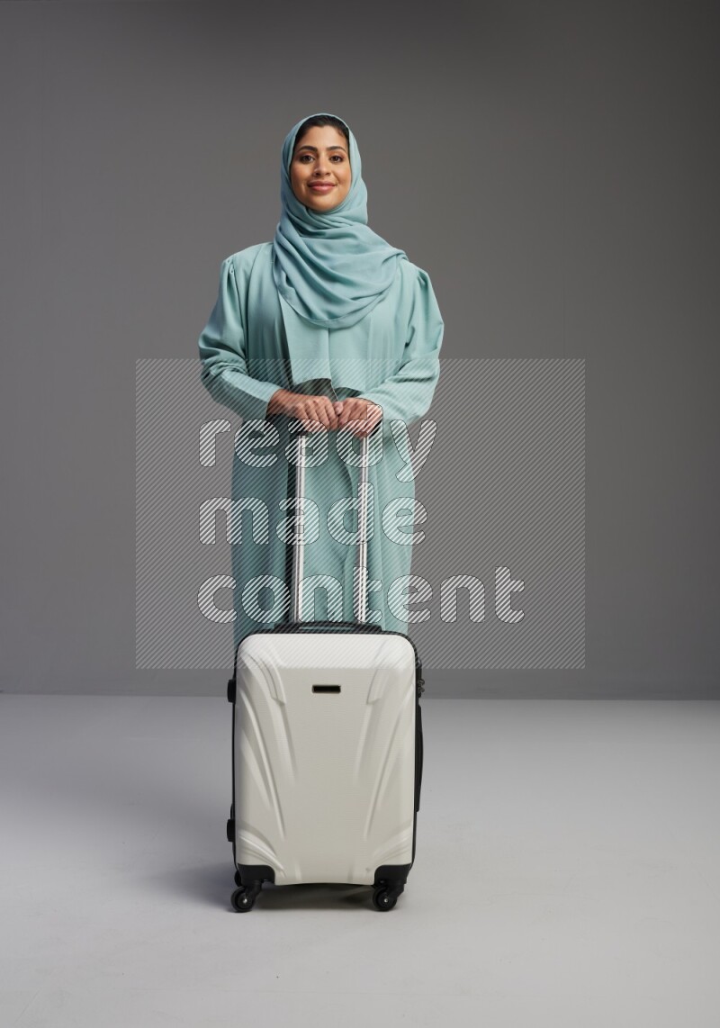 Saudi Woman wearing Abaya standing holding Travel bag on Gray background