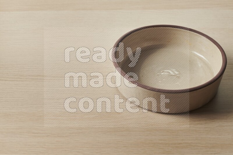 A beige pottery oven bowl on light wooden background