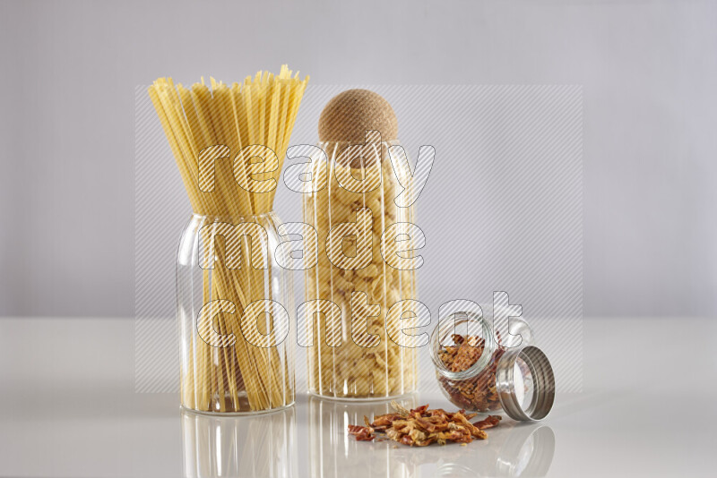 Raw pasta in glass jars with chilis on light grey background