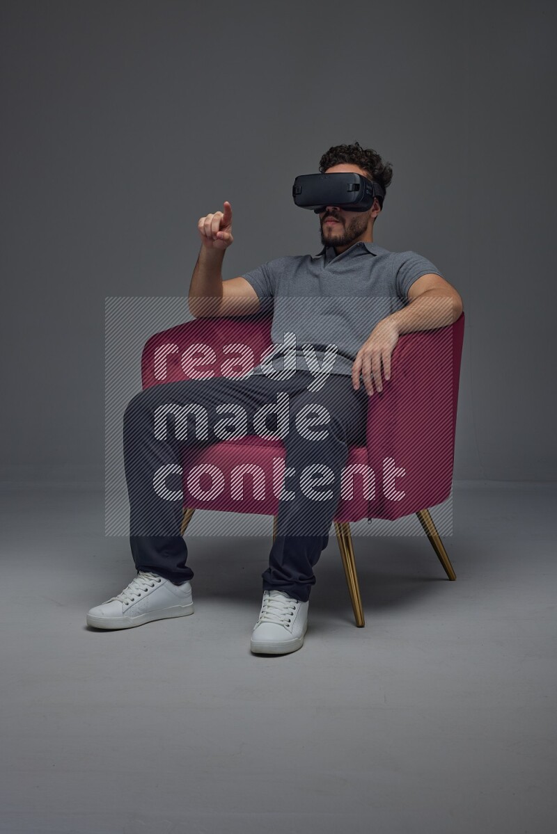 A man wearing casual and wearing VR while sitting on a burgundy chair eye level on a gray background
