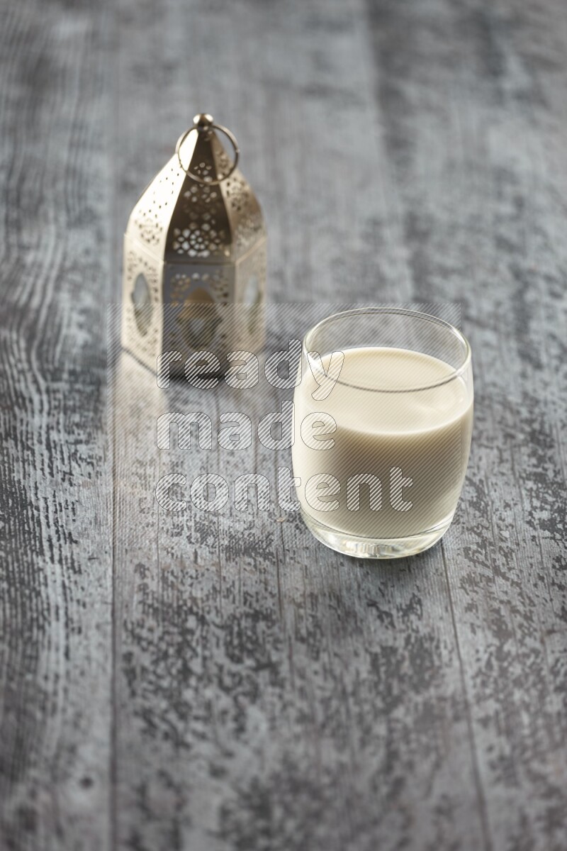 A silver lantern with different drinks, dates, nuts, prayer beads and quran on grey wooden background