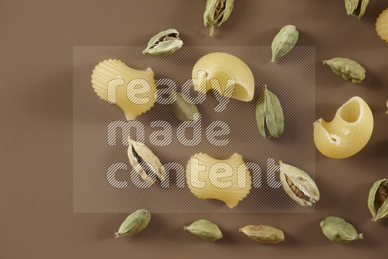 Raw pasta with different ingredients such as cherry tomatoes, garlic, onions, red chilis, black pepper, white pepper, bay laurel leaves, rosemary and cardamom on beige background