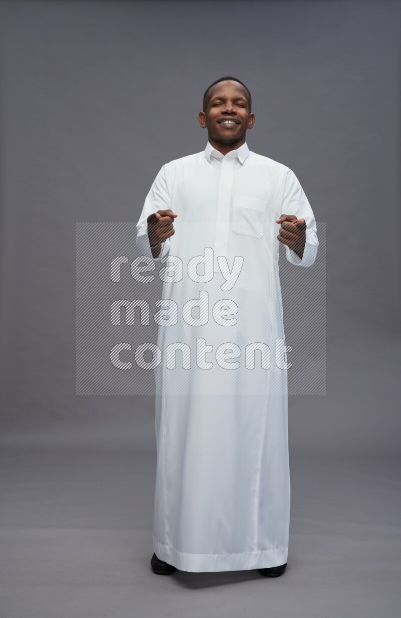 Saudi man wearing thob standing interacting with the camera on gray background