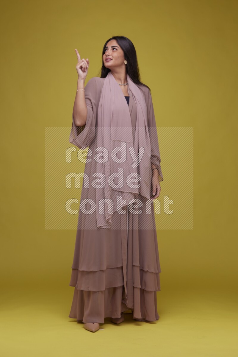 A woman Pointing on a Yellow Background wearing Brown Abaya