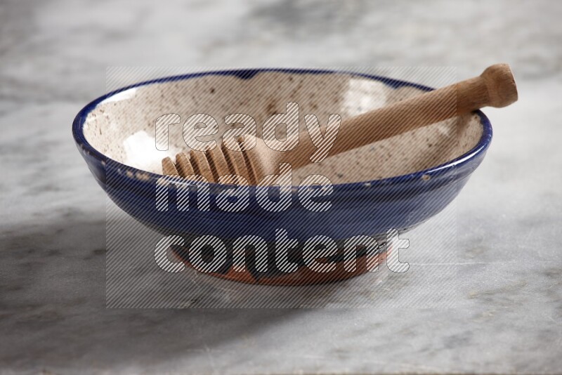 Multicolored pottery bowl with wooden honey dipper in it on grey marble background