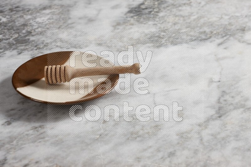 Multicolored pottery plate with wooden honey dipper in it on grey marble background