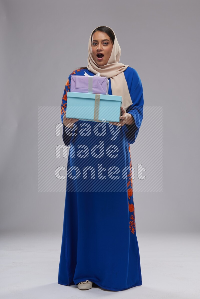 A Saudi woman standing wearing Jalabeya holding a gift box
