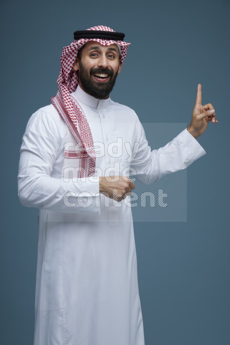 A man pointing in a blue background wearing Saudi Thob and Shomag