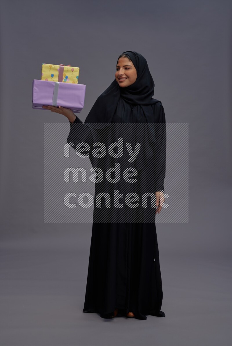 Saudi woman wearing Abaya standing holding gift box on gray background