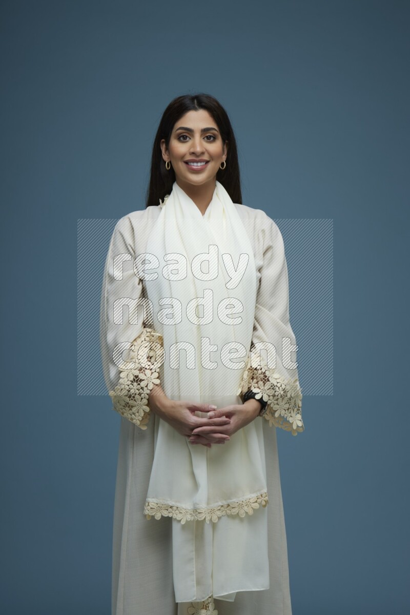 A Saudi woman posing in a blue background wearing an off-white Abaya no Hijab