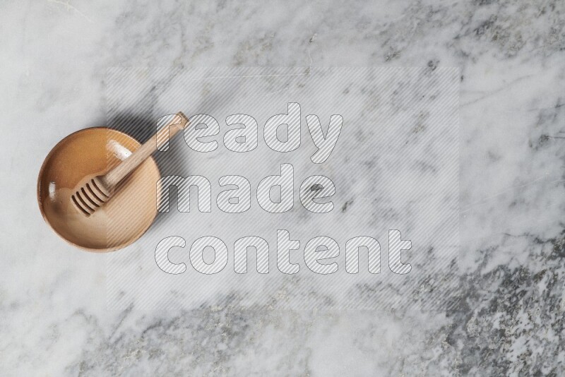 طبق فخاري متعدد الألوان مع ملعقة عسل خشبية بداخله على خلفية من الرخام الرمادي